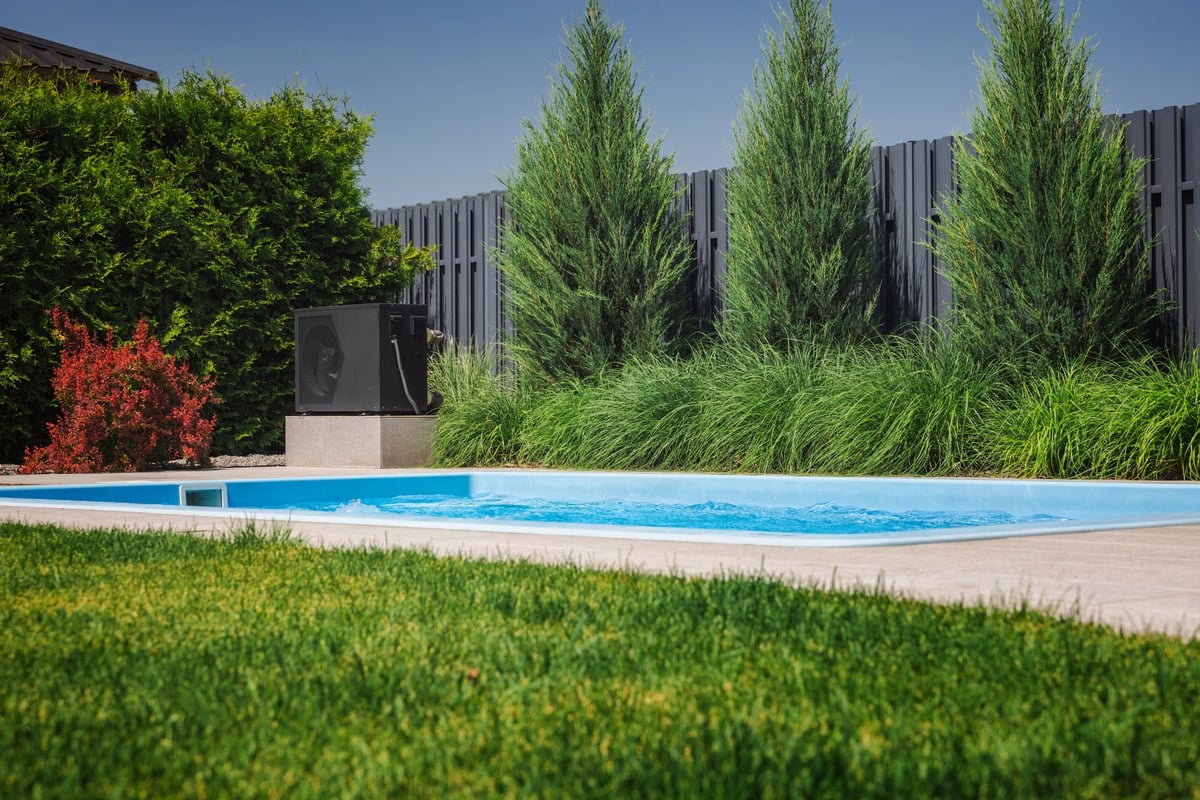 Modern heat pump next to backyard pool with landscaped garden