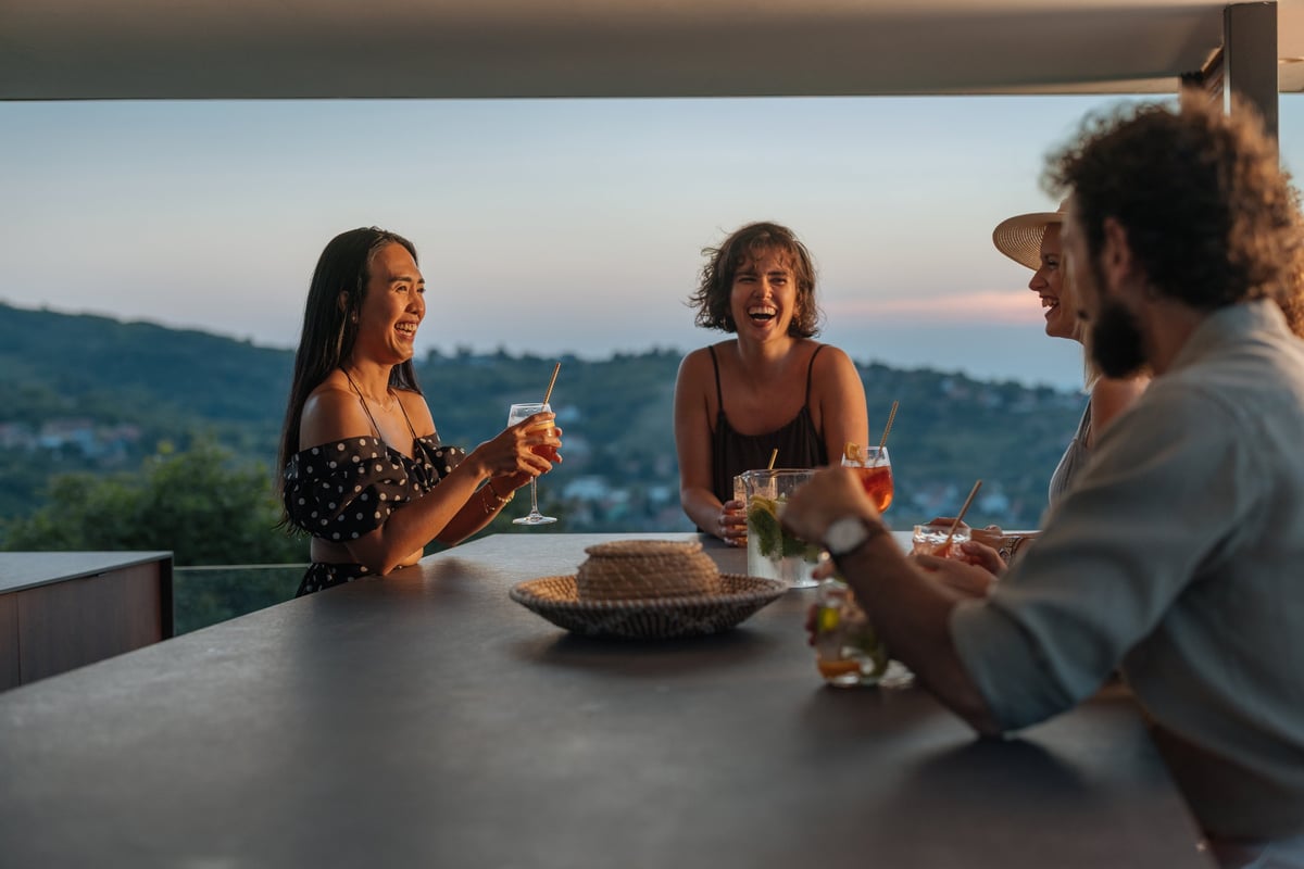 Friends laughing and having drinks on a modern terrace with sunset view